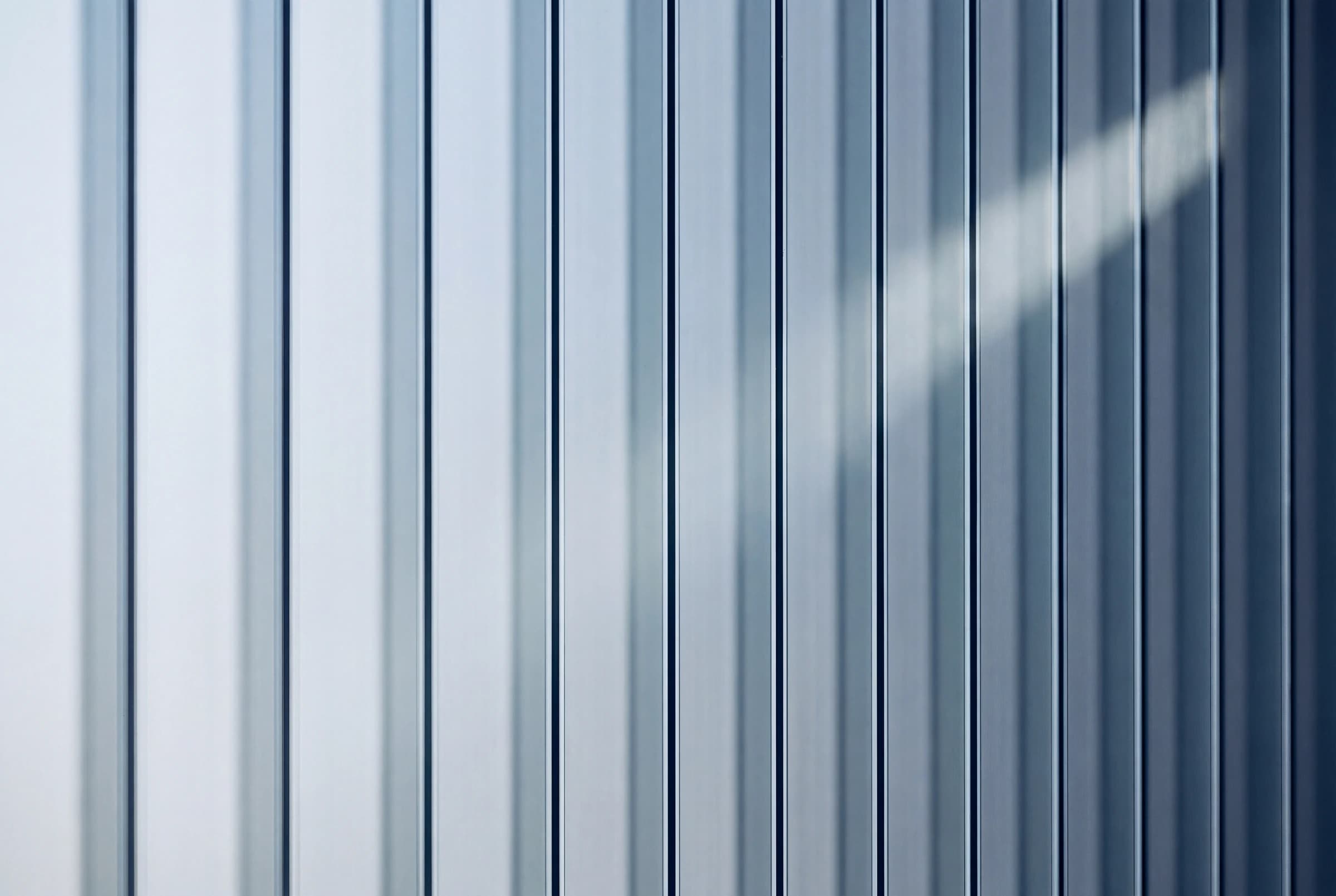 Cool daylight divided into precise parallel bands by a wall of vertical fluted glass
