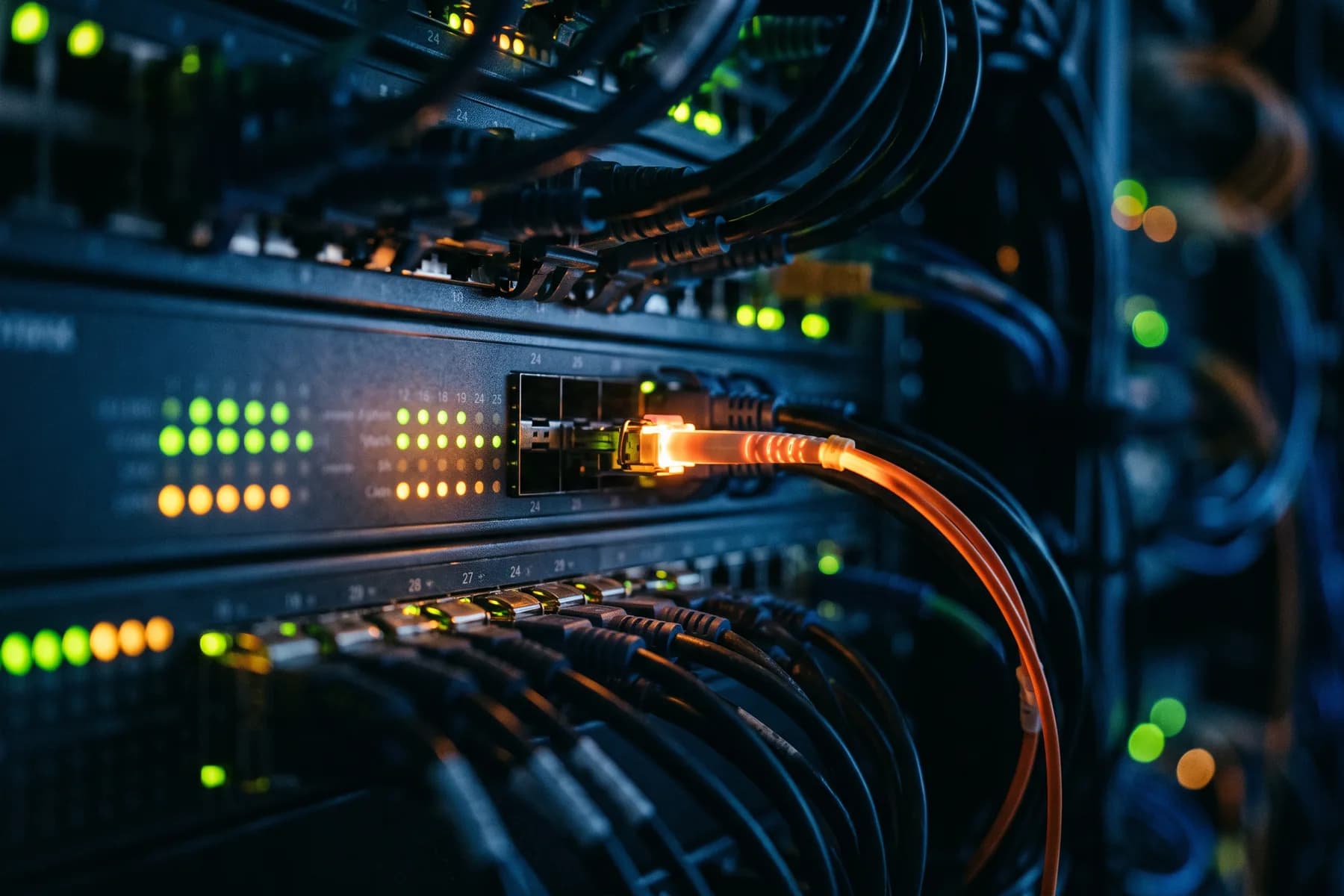 Network cables patched into a switch in a dark room, indicator lights burning green and amber