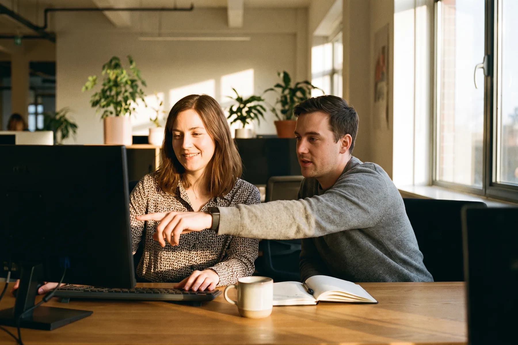 Two colleagues working through something together at a screen in warm afternoon light